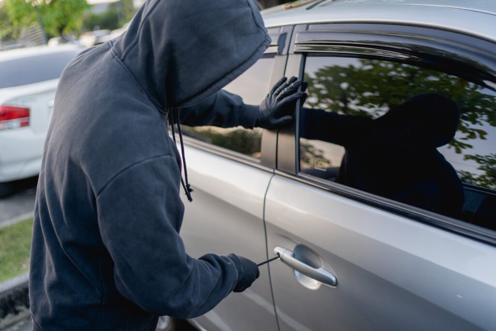 Hooded person attempting to break into a vehicle in a parking lot